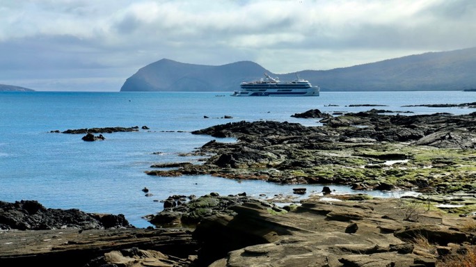 Rocky Galápagos coastline with a calm sea and an island in the distance
